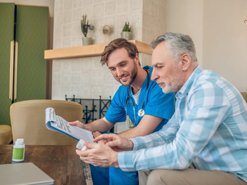 Smiling doctor with a blank form looking at a plastic bottle in his patient hands